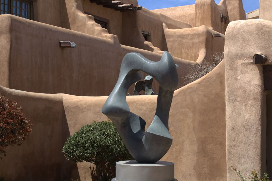 Modern abstract sculpture set against Santa Fe's iconic Pueblo Revival architecture, showcasing earthy tones.